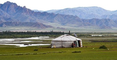 Familie steht vor einer Jurte in einer Wiesen Landschaft