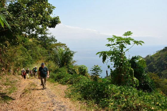 Eine Gruppe Wanderer kommt bergaufwärts auf den Betrachter zu. Die Hänge sind mit grüner Vegetation bewachsen. Rechts im Bildmittelgrund eröffnet sich die Sicht in den blauen Himmel.