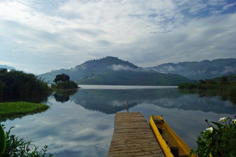 Lake Bunyoni in Uganda mit Blick auf einen Steg mit Boot und im Hintergrund Berge