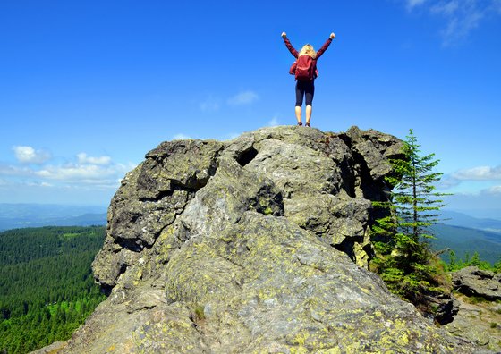 Eine Frau steht triumphierend auf einem Felsen im Bayerischen Wald. 