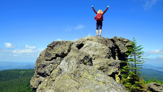Eine Frau steht triumphierend auf einem Felsen im Bayerischen Wald. 