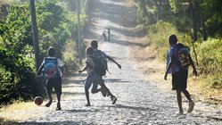 Kinder mit Schulrucksäcken spielen Fußball auf der Straße.