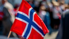 Im Vordergrund sieht man die norwegische Flagge, im Hintergrund verschwommene Menschen.