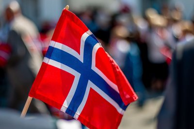 Im Vordergrund sieht man die norwegische Flagge, im Hintergrund verschwommene Menschen.