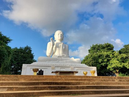 Am Kopf einer Treppe steht eine große weiße Buddha-Skulptur.