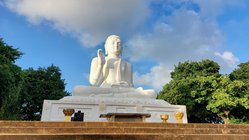 Am Kopf einer Treppe steht eine große weiße Buddha-Skulptur.