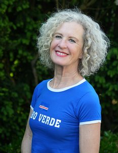 Eine Frau mit grau gelockten Haaren und blauem T-Shirt mit der Aufschrift "Cabo Verde" lächelt in die Kamera.