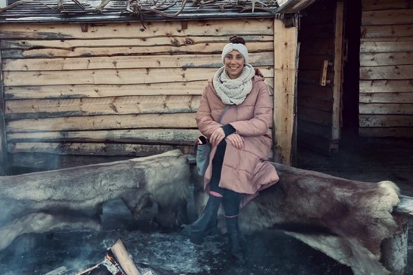 Ein Foto von unserer contrastravel Reiseberaterin, wie sie in einer dicken Jacke auf einem Baumstamm am Lagerfeuer sitzt.