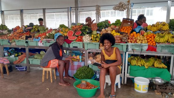 Zwei Frauen sitzen vor einem Obst- und Gemüsestand auf einem Markt in Praia, Santiago