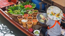 Eine Frau verkauft buntes Obst und gemüse in einem Boot auf einem schwimmenden Markt in Thailand.