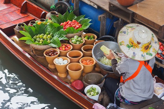 Eine Frau verkauft buntes Obst und gemüse in einem Boot auf einem schwimmenden Markt in Thailand.