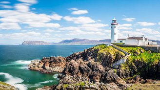 Leuchtturm auf einer Klippe in Irland, umgeben von dem Atlantischen Ozean und steilen Felswänden.