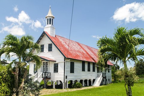 weiße Holzkirche mit kleinem Glockenturm auf dem Dach umgeben von ein paar Palmen
