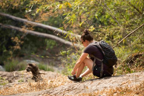 auf dem Boden sitzende Frau mit Rucksack bindet sich die Schuhe