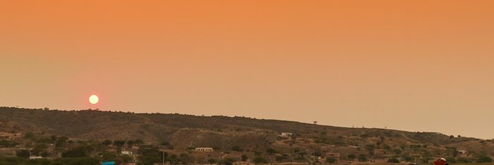 Einheimische Frauen laufen bei Sonnenuntergang mit Wannen auf dem Kopf eine Straße an einem Gewässer entlang