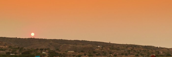 Einheimische Frauen laufen bei Sonnenuntergang mit Wannen auf dem Kopf eine Straße an einem Gewässer entlang