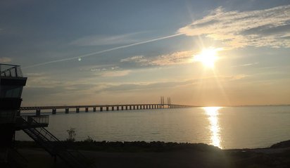 Von links zieht sich eine Brücke in das Meer bis tief in den Bildmittelgrund. Eine fahle, tiefstehende Sonne beleuchtet die Meeresszene.