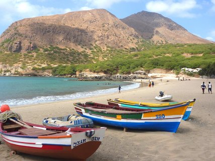 Bunte Boote liegen an einem Sandstrand mit einem Berg im Hintergrund.