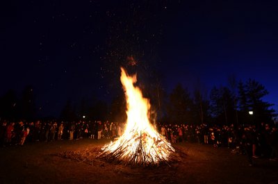 Um ein Lagerfeuer stehen viele Menschen, um die Walpurgisnacht zu feiern.