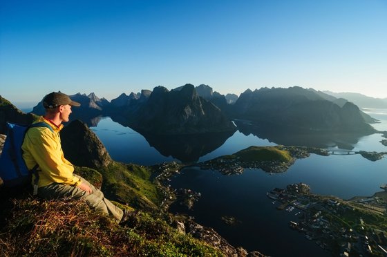 Auf dem Bild ist ein Wanderer zu sehen, der einen wunderschönen Ausblick auf eine Fjordstadt und dem dazugehörigen Fjord hat.