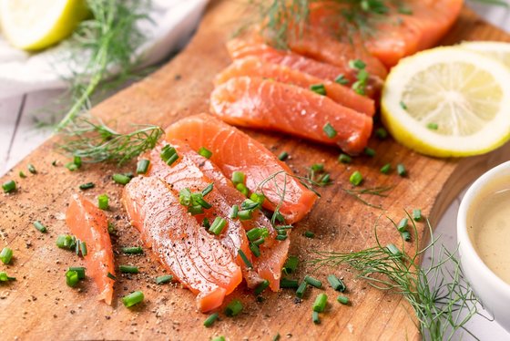 Gravad Lachs aus Schweden Auf einem Holzbrett sind einige Stücke aufgeschnittenen Lachses mit Kräutern und Zitronenscheiben arrangiert.