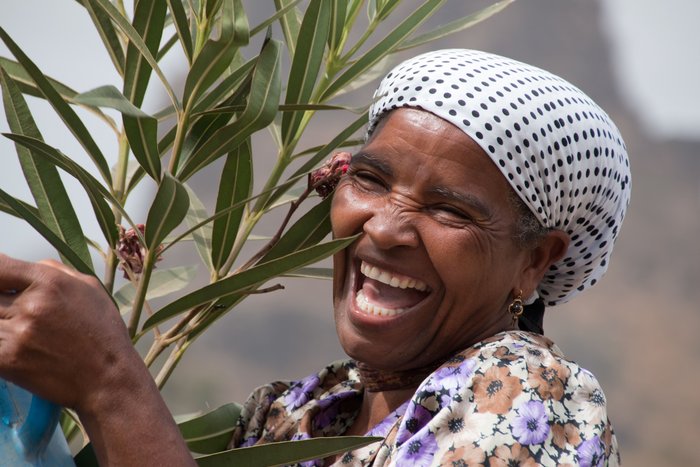 Eine lachende, einheimische Frau trägt eine Oleanderpflanze