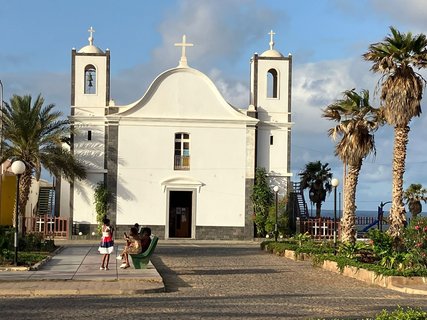 Man sieht die weiße Fassade einer schlichten Kirche.