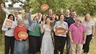 Das Team von REISEN MIT SINNEN steht jubelnd für ein Gruppenbild auf einer Wiesen- und Waldlandschaft. 