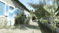 Man sieht eine mit Kopfsteinpflaster belegte Straße, die auf der rechten Seite von einer Bruchsteinmauer eingefasst ist, links der Straße erstreckt sich eine Häuserzeile ebenfalls aus groben Steinen erbaut.