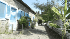 Man sieht eine mit Kopfsteinpflaster belegte Straße, die auf der rechten Seite von einer Bruchsteinmauer eingefasst ist, links der Straße erstreckt sich eine Häuserzeile ebenfalls aus groben Steinen erbaut.