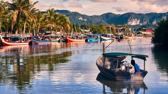 Ein Fischerboot fährt auf einen palmenumsäumten Hafen in Langkawi in Malaysia zu.