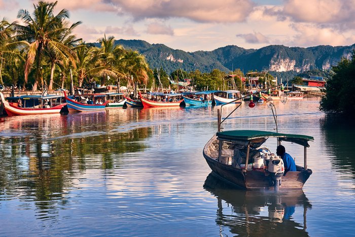 Ein Fischerboot fährt auf einen palmenumsäumten Hafen in Langkawi in Malaysia zu.