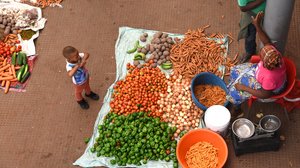 Kind vor dem Marktstand einer Frau, die frisches Gemüse auf den Kapverden verkauft.