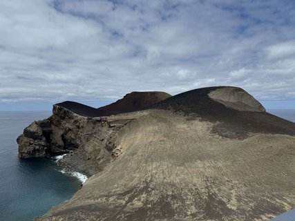 Eine grau-schwarze Landzunge aus Vulkangestein erstreckt sich in das dunkelblaue Meer.