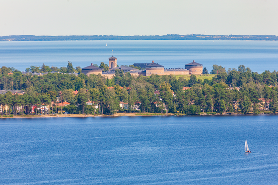 Sug einer baumbestandenen Insel in einer weiten Wasserfläche erhebt sich eine große FEstungsanlage.
