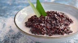 Nahaufnahme einer Schale mit Bubur Ketan Hitam, einem indonesischen Dessert aus schwarzem Klebreis, garniert mit einer hellen Kokoscreme, serviert auf einem Tisch