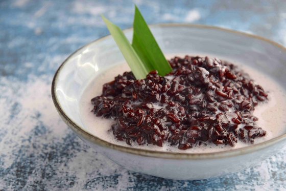 Nahaufnahme einer Schale mit Bubur Ketan Hitam, einem indonesischen Dessert aus schwarzem Klebreis, garniert mit einer hellen Kokoscreme, serviert auf einem Tisch