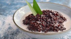 Nahaufnahme einer Schale mit Bubur Ketan Hitam, einem indonesischen Dessert aus schwarzem Klebreis, garniert mit einer hellen Kokoscreme, serviert auf einem Tisch