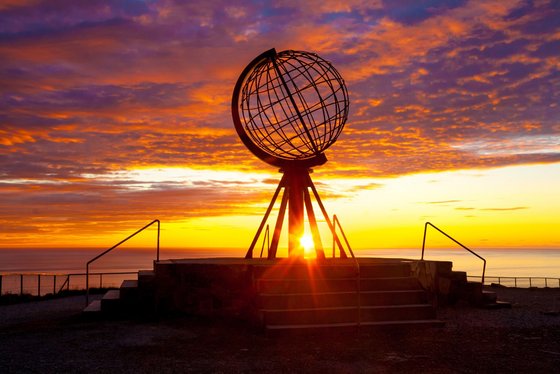 Mitternachtssonne am Nordkap in Norwegen Die Mitternachtssonne stahlt durch einen Globus am Nordkap