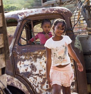 Zwei einheimische Mädchen vor einem alten, rostigen Auto 