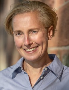 Portrait einer einer etwa 50-jährigen Frau mit kurzen blonden Haaren, die frontal in die Kamera lächelt.