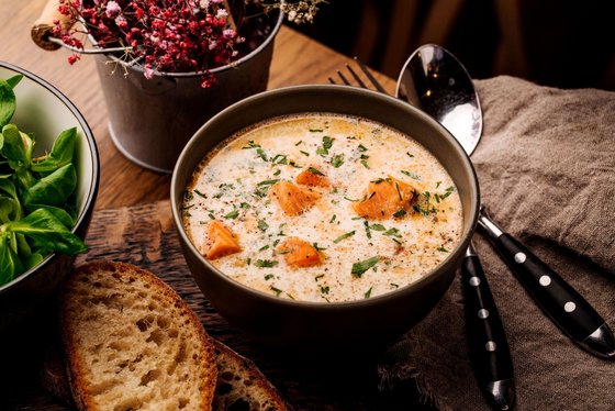 Suppe mit Lachs ist eine begehrte Winterspeise Um eine Schüssel mit Lachssuppe sind eine Brotscheibe und Kräuter arrangiert.