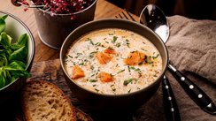 Um eine Schüssel mit Lachssuppe sind eine Brotscheibe und Kräuter arrangiert.