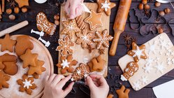 Drei Hände verzieren Lebkuchen auf einem Holzbrett mit Zuckerguss