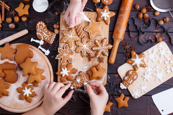 Drei Hände verzieren Lebkuchen auf einem Holzbrett mit Zuckerguss