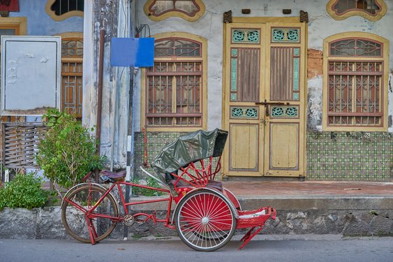 Typisch Malaysia: Rikscha in den Straßen von Penang Eine rote Rikscha steht am Straßenrand vor alten Gebäuden in Penang.
