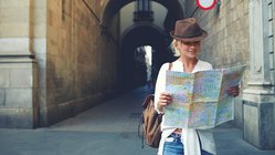 Eine Reisende sieht zwischen alten Gebäuden auf eine Stadtkarte