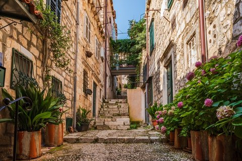 Schmale, gepflasterte Gasse in der Altstadt von Dubrovnik, Kroatien. Hohe Steinmauern säumen den Weg, während warme Lichtreflexe die Treppenstufen erhellen.