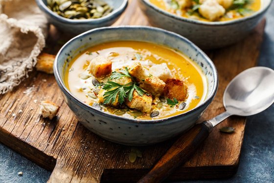 Eine Schale cremige vegane Kürbissuppe mit Orangenscheiben, Ingwer und knusprigen Brotcroutons, perfekt angerichtet für den Herbst.