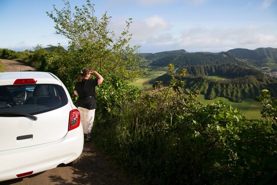 Mit dem Mietwagen durch die Azoren Ein Frau steht neben einem Mietwagen und blickt auf die Landschaft der Azoren